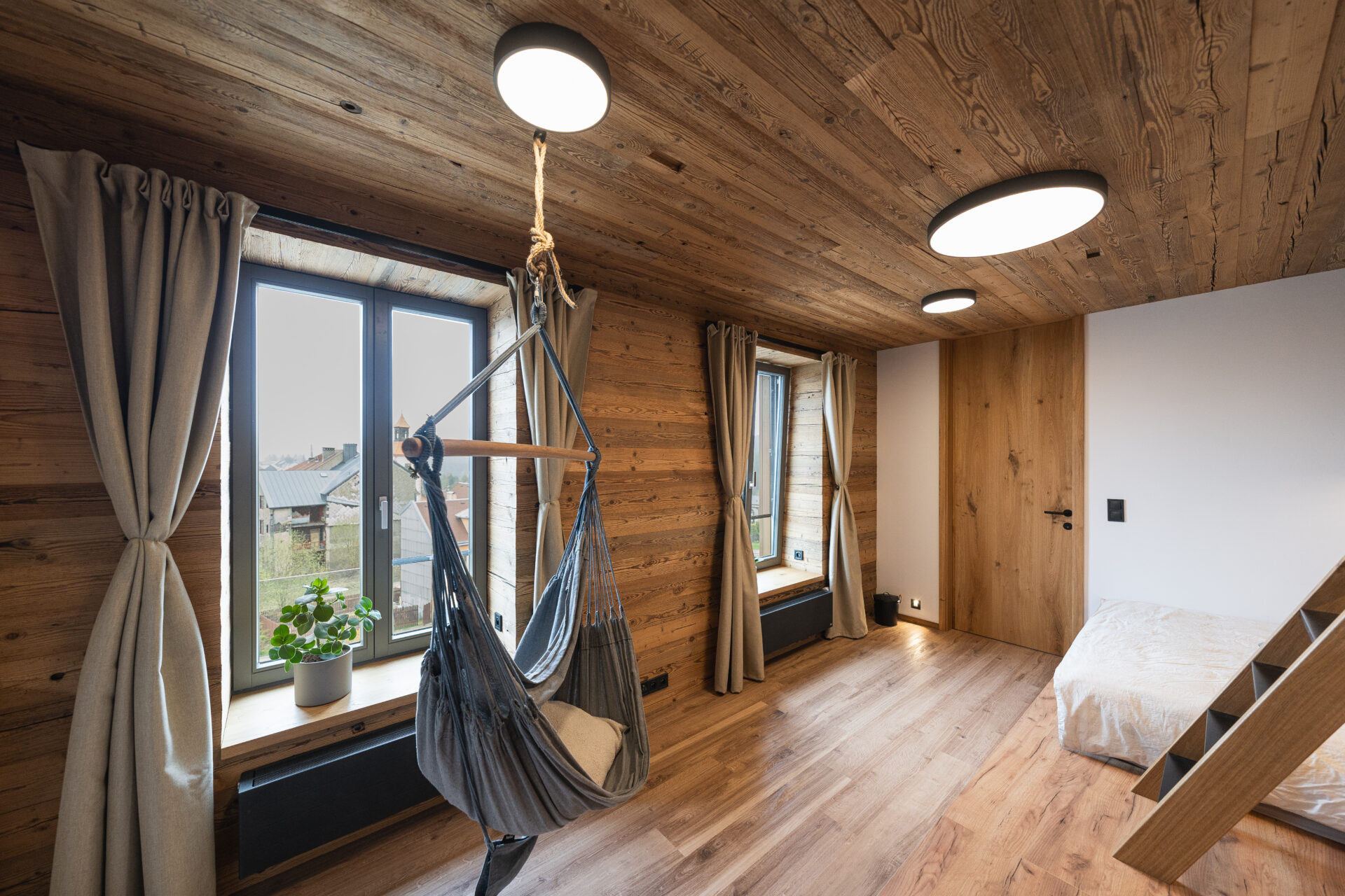 Pokoj apartmánu v&nbsp;Abertamech s&nbsp;dřevěnými obklady a&nbsp;závěsným křeslem. Inspirace od&nbsp;REMY Design.